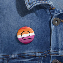 Close-up of a white circular pride button featuring the Libra zodiac glyph centered over a lesbian pride flag background in oranges, white, and pinks attached to a blue denim jacket at the right chest with the button clearly visible.