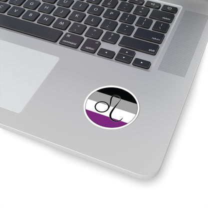 Close-up of the bottom right corner of a silver laptop featuring a 2 inch by 2 inch circular zodiac sticker with a centered Leo glyph on an Asexual pride flag style background applied to the surface.