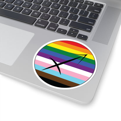 Close-up of the bottom right corner of a silver laptop featuring a 4 inch by 4 inch circular zodiac sticker with a centered Sagittarius glyph on a progress pride flag style background applied to the surface.