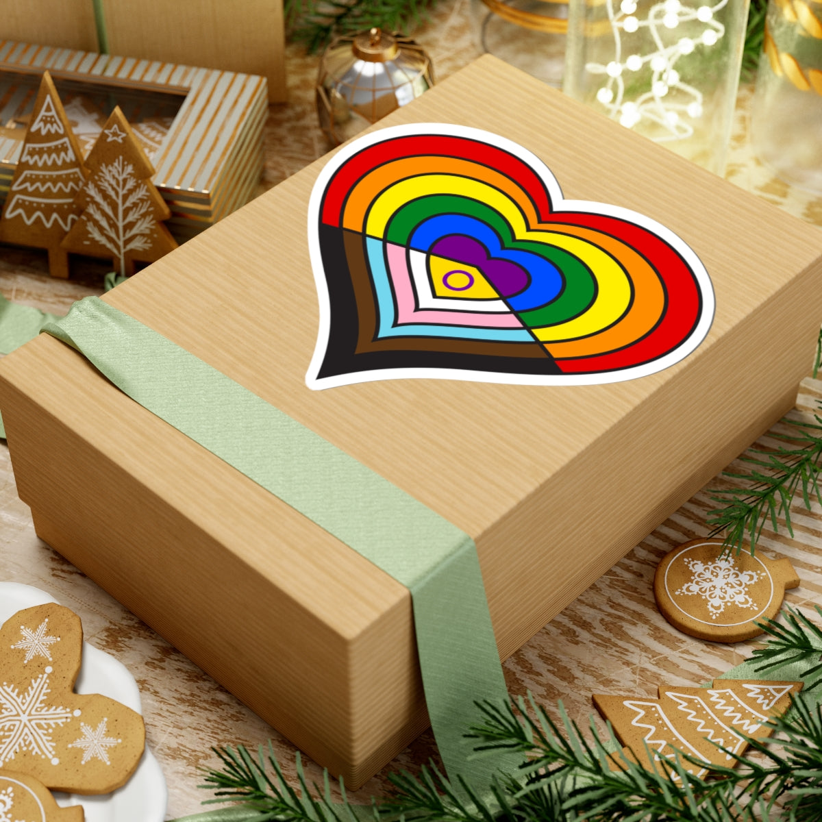 Gift box with a green ribbon on a festive background with cookies and Christmas decorations. Heart-shaped Intersex-inclusive progress pride sticker centered on the box.