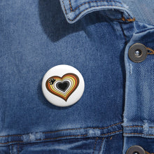 Close-up of a white circular pride button featuring a nested heart design inspired by the Bear pride flag in browns, cream, white, grey and black, attached to a blue denim jacket at the right chest with the button clearly visible.