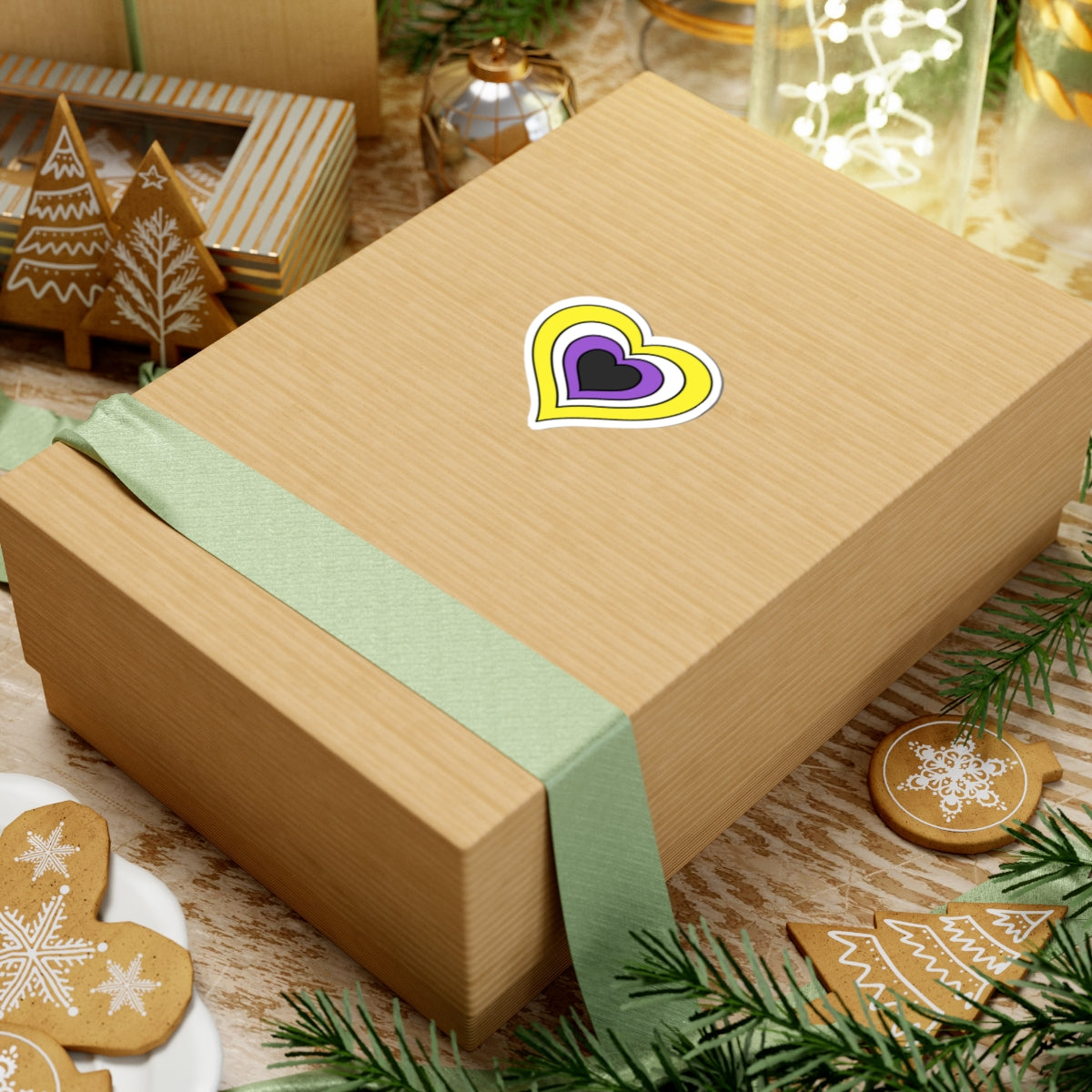 Gift box with a green ribbon on a festive background with cookies and Christmas decorations. Heart-shaped Nonbinary pride sticker centered on the box.