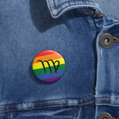 Close-up of a white circular pride button featuring the Virgo zodiac glyph centered over a rainbow pride flag background in red, orange, yellow, green, blue, and purple, attached to a blue denim jacket at the right chest with the button clearly visible.