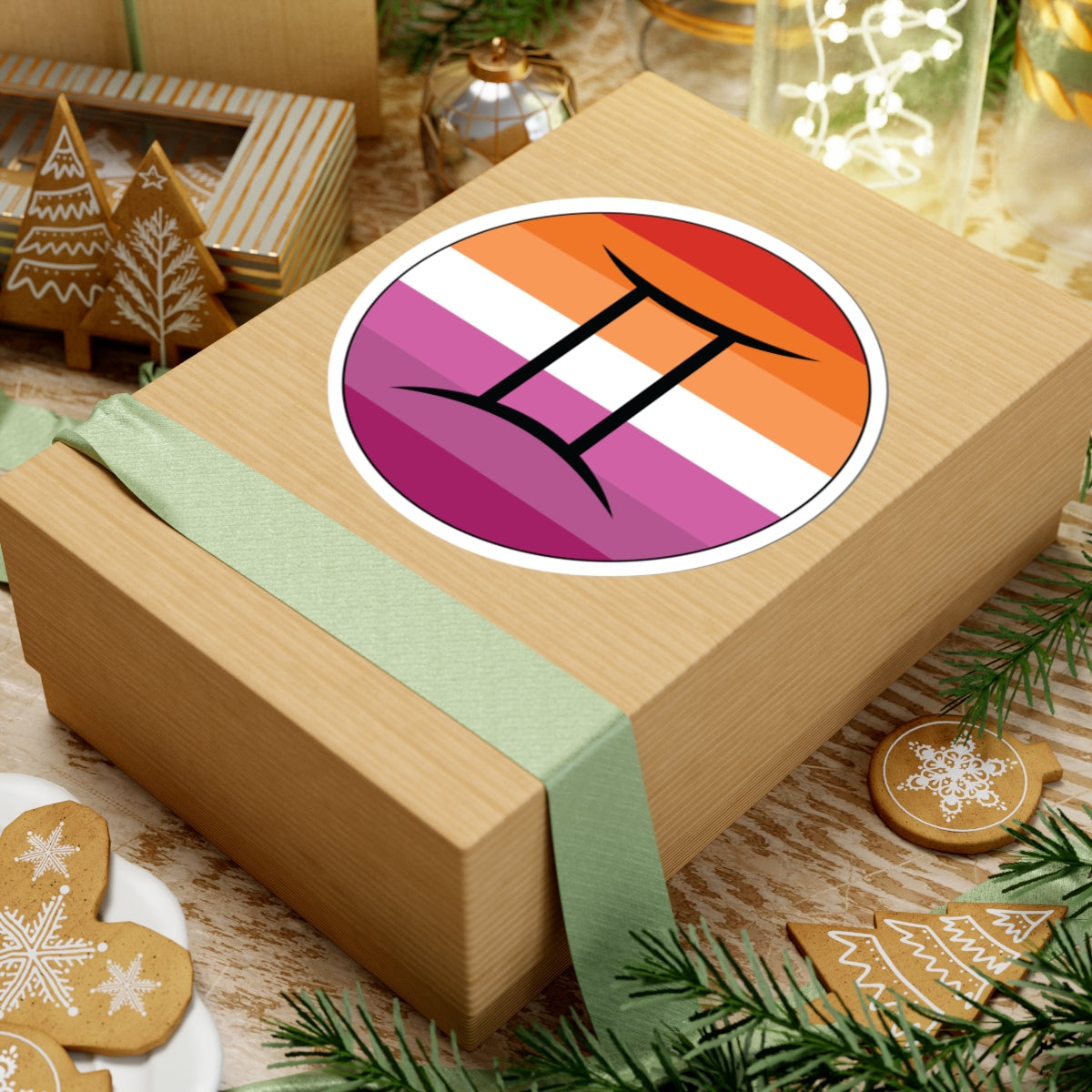 Gift box with a green ribbon on a festive background with cookies and Christmas decorations. Gemini Lesbian pride sticker centered on the box.