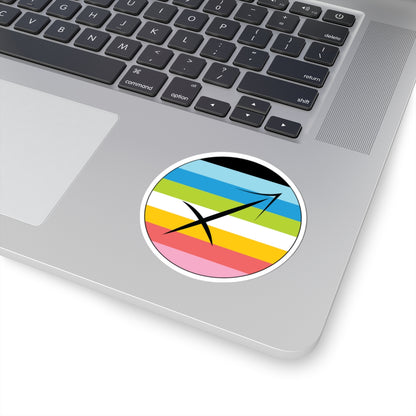 Close-up of the bottom right corner of a silver laptop featuring a 3 inch by 3 inch circular zodiac sticker with a centered Sagittarius glyph on a Queer pride flag style background applied to the surface.