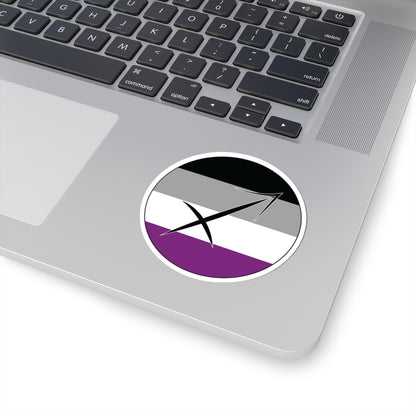 Close-up of the bottom right corner of a silver laptop featuring a 3 inch by 3 inch circular zodiac sticker with a centered Sagittarius glyph on an Asexual pride flag style background applied to the surface.