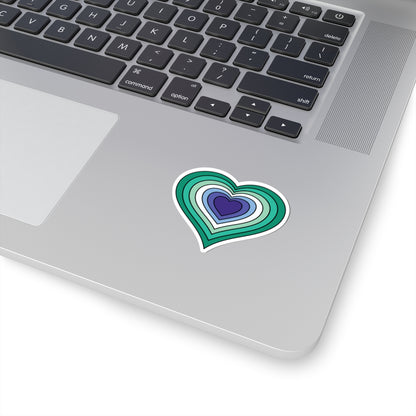 Close-up of the bottom right corner of a silver laptop featuring a 2 inch by 2 inch pride flag heart sticker in a Gay Men flag style applied to the surface.