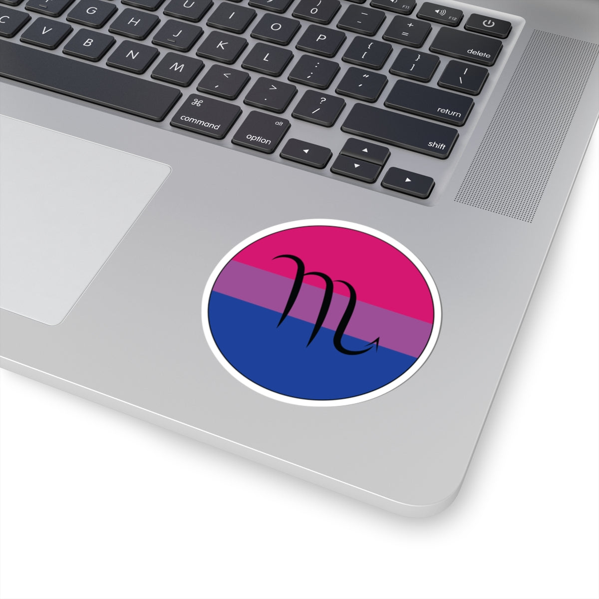 Close-up of the bottom right corner of a silver laptop featuring a 3 inch by 3 inch circular zodiac sticker with a centered Scorpio glyph on a Bisexual pride flag style background applied to the surface.