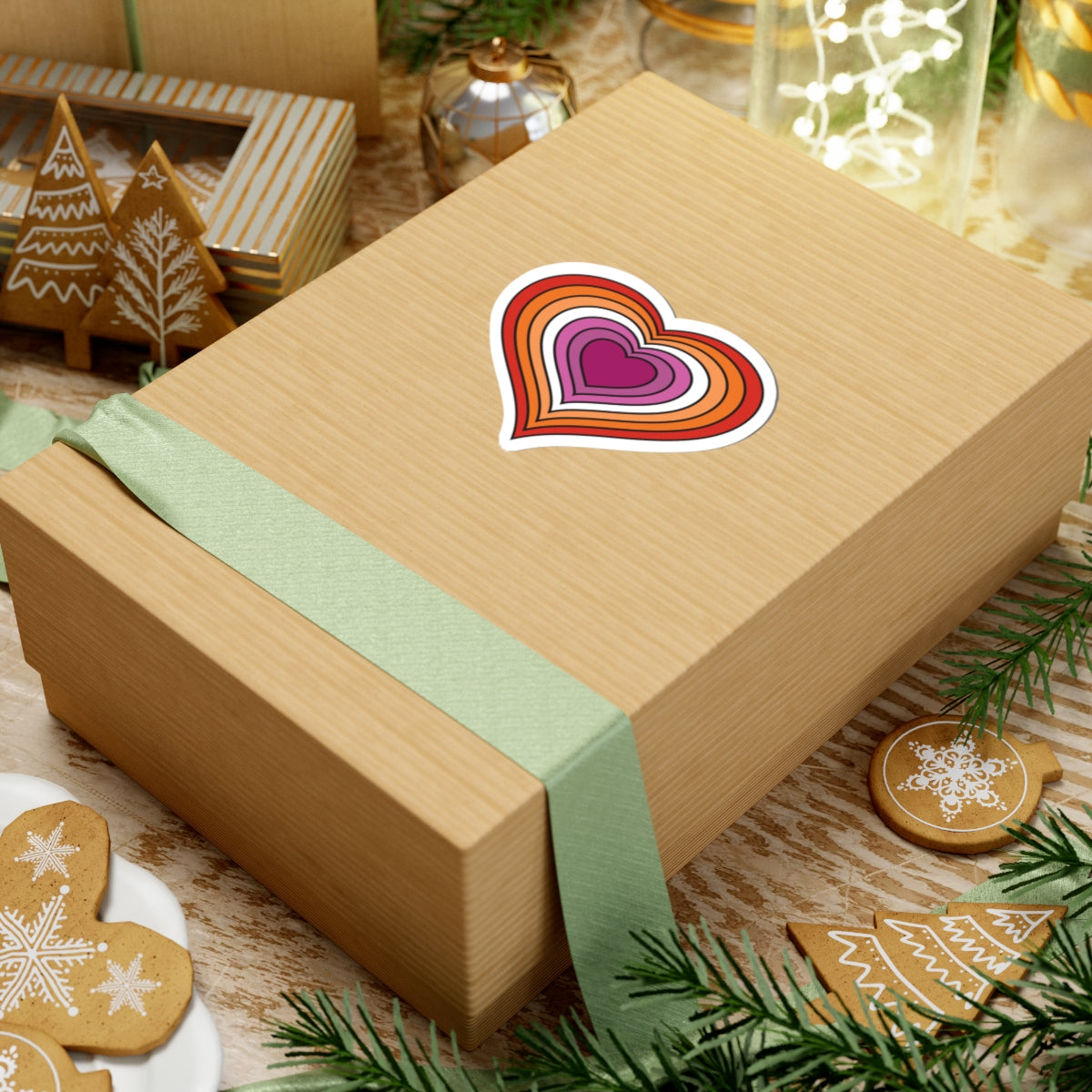 Gift box with a green ribbon on a festive table with cookies and decorations. Lesbian heart sticker centered on the box.
