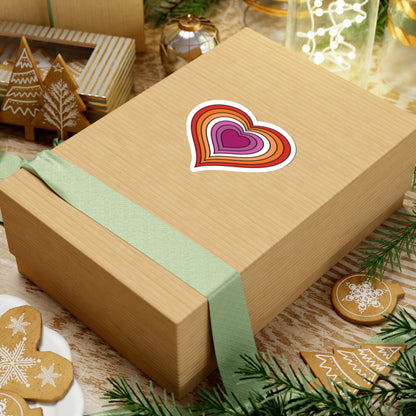 Gift box with a green ribbon on a festive table with cookies and decorations. Lesbian heart sticker centered on the box.