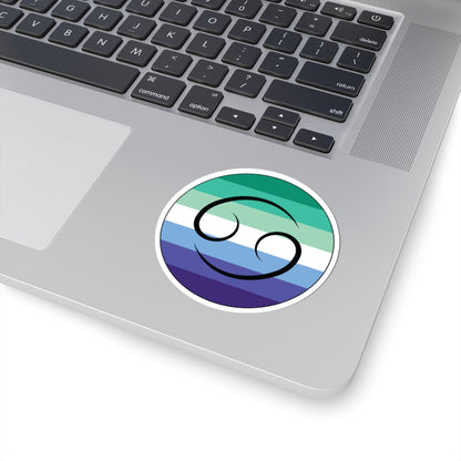Close-up of the bottom right corner of a silver laptop featuring a 3 inch by 3 inch circular zodiac sticker with a centered Cancer glyph on a Gay Men pride flag style background applied to the surface.