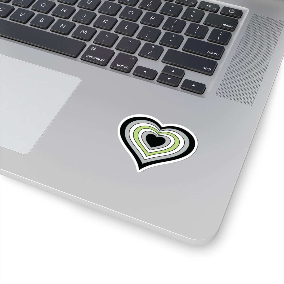 Close-up of the bottom right corner of a silver laptop featuring a 2 inch by 2 inch pride flag heart sticker in an Agender flag style applied to the surface.