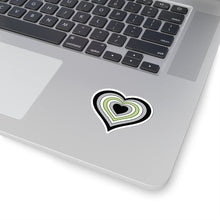 Close-up of the bottom right corner of a silver laptop featuring a 2 inch by 2 inch pride flag heart sticker in an Agender flag style applied to the surface.