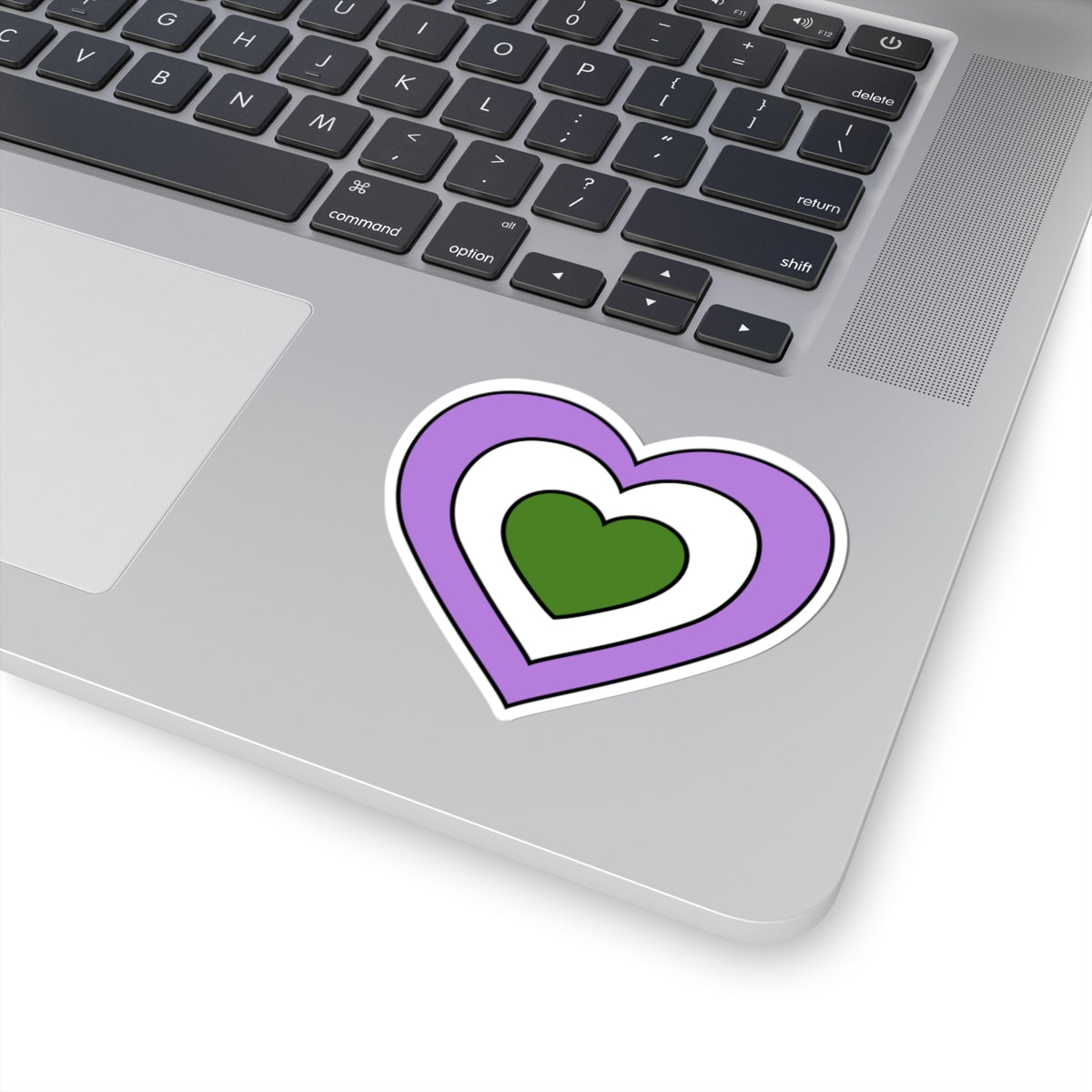 Close-up of the bottom right corner of a silver laptop featuring a 3 inch by 3 inch pride flag heart sticker in a Genderqueer flag style applied to the surface.