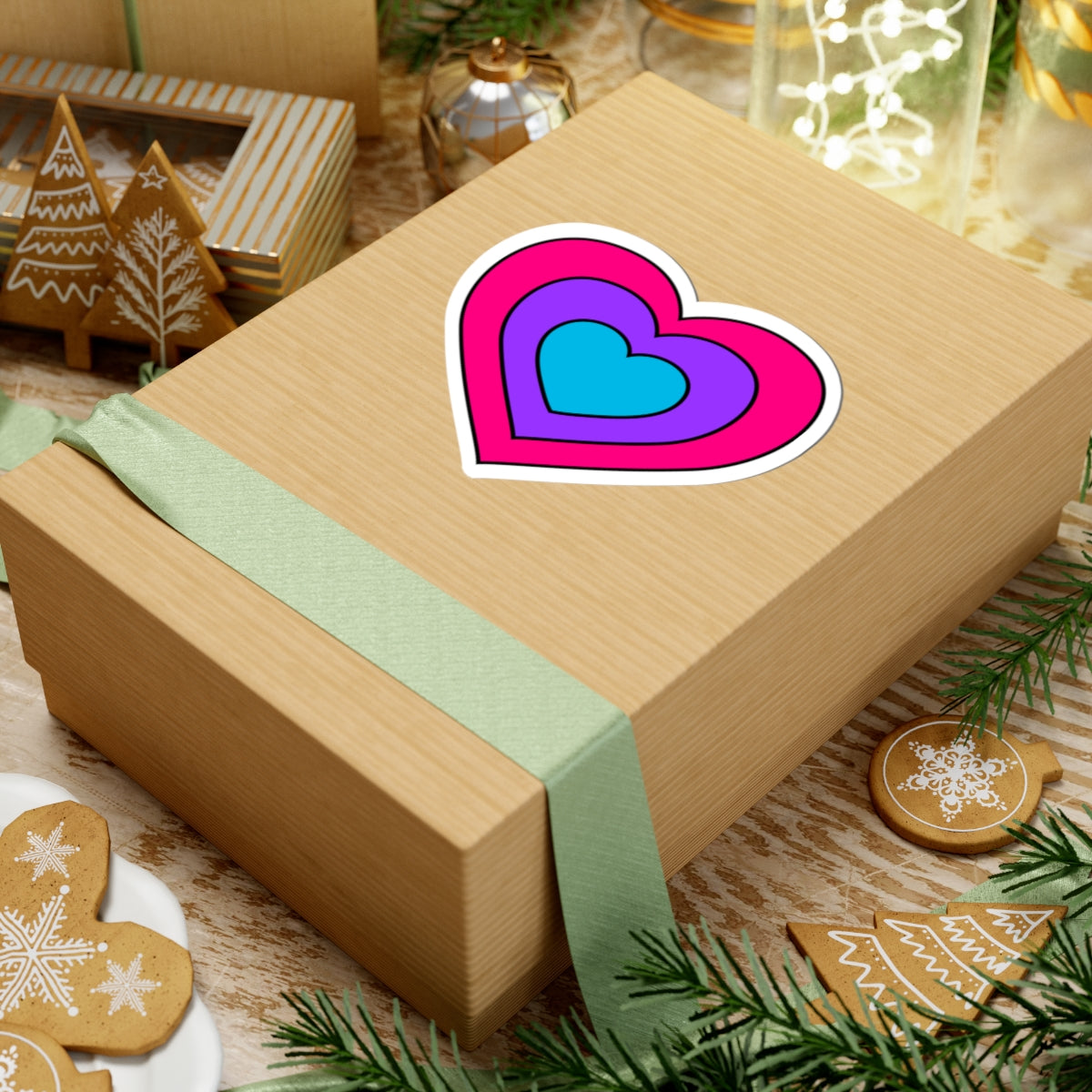 Gift box with a green ribbon on a festive background with cookies and Christmas decorations. Heart-shaped Androgyne pride sticker centered on the box.