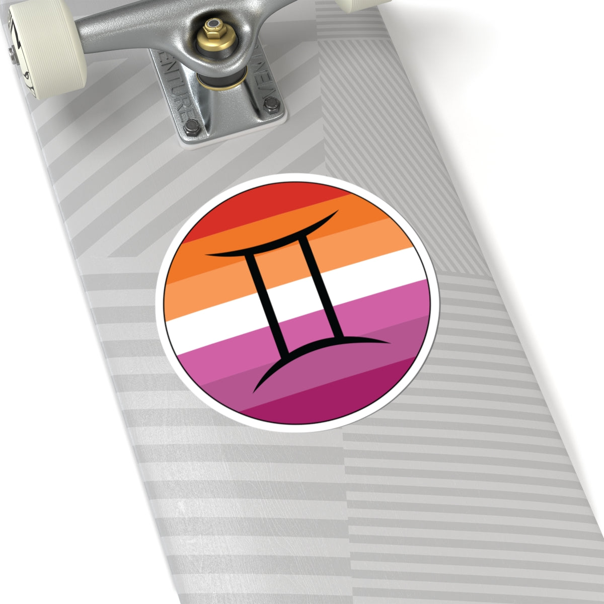 Close-up of the bottom of a silver skateboard featuring a 6 inch by 6 inch circular zodiac sticker with a centered Gemini glyph on a Lesbian pride flag style background applied to the surface.