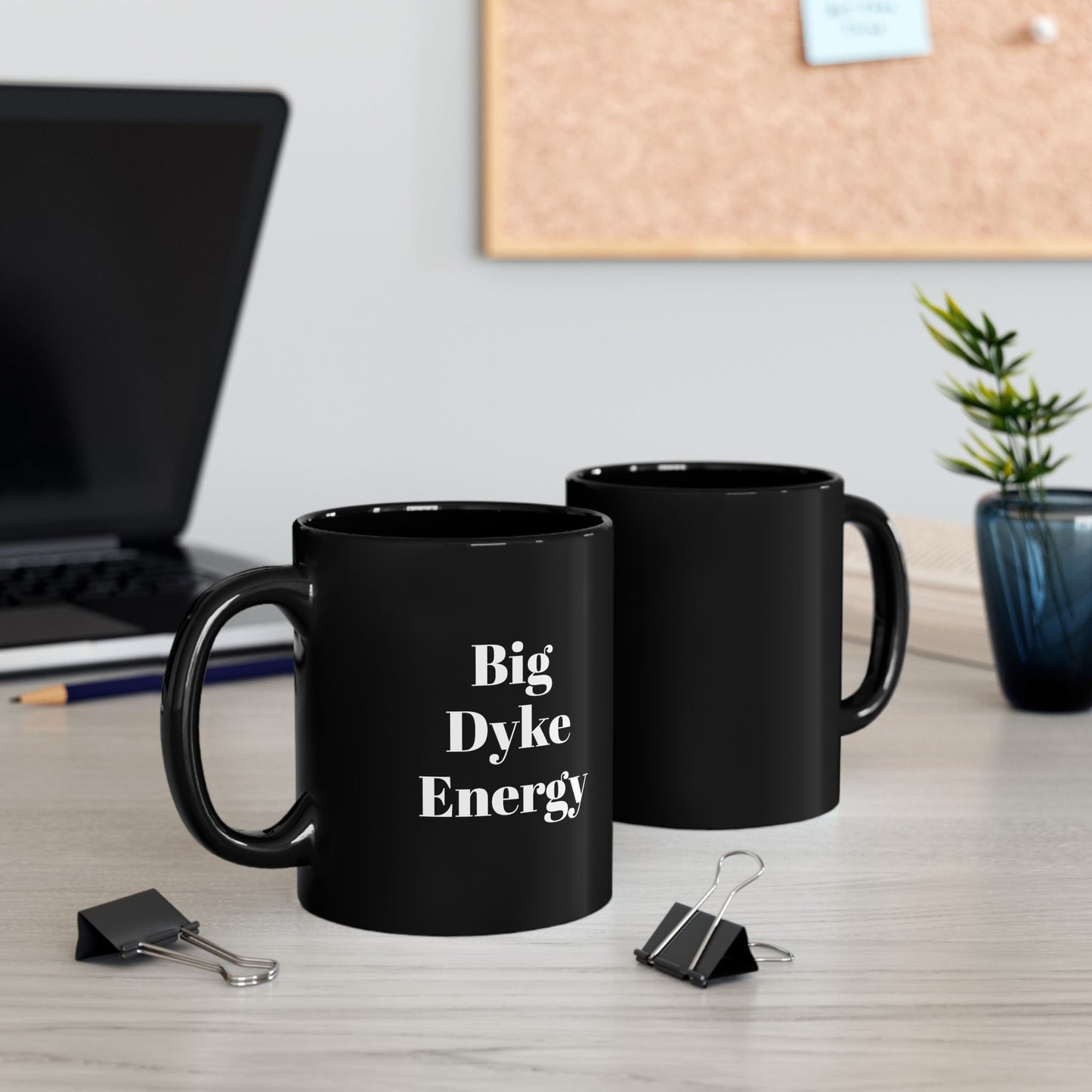 Black mugs with 'Big Dyke Energy' text on a desk with office supplies.