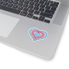 Close-up of the bottom right corner of a silver laptop featuring a 2 inch by 2 inch pride flag heart sticker in a Transfem flag style applied to the surface.