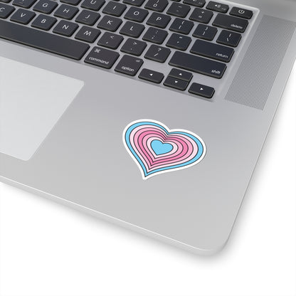 Close-up of the bottom right corner of a silver laptop featuring a 2 inch by 2 inch pride flag heart sticker in a Transfem flag style applied to the surface.