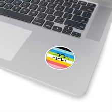 Close-up of the bottom right corner of a silver laptop featuring a 2 inch by 2 inch circular zodiac sticker with a centered Aquarius glyph on a Queer pride flag style background applied to the surface.