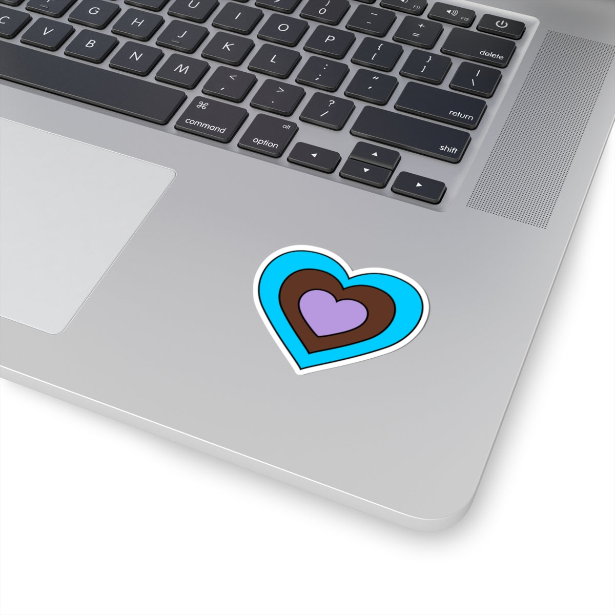 Close-up of the bottom right corner of a silver laptop featuring a 2 inch by 2 inch pride flag heart sticker in an Androsexual flag style applied to the surface.