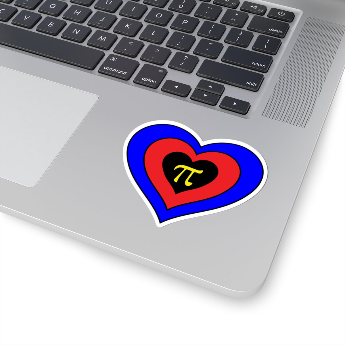 Close-up of the bottom right corner of a silver laptop featuring a 3 inch by 3 inch pride flag heart sticker in a Polyamory flag style applied to the surface.