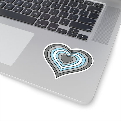 Close-up of the bottom right corner of a silver laptop featuring a 3 inch by 3 inch pride flag heart sticker in a Demiboy flag style applied to the surface.