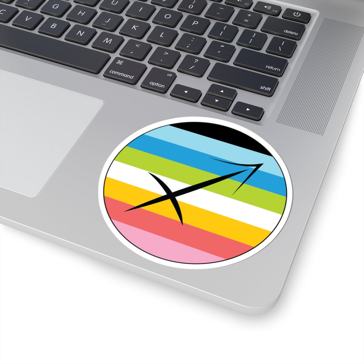 Close-up of the bottom right corner of a silver laptop featuring a 4 inch by 4 inch circular zodiac sticker with a centered Sagittarius glyph on a Queer pride flag style background applied to the surface.