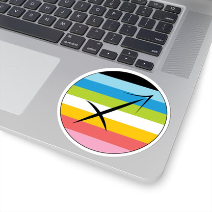 Close-up of the bottom right corner of a silver laptop featuring a 4 inch by 4 inch circular zodiac sticker with a centered Sagittarius glyph on a Queer pride flag style background applied to the surface.