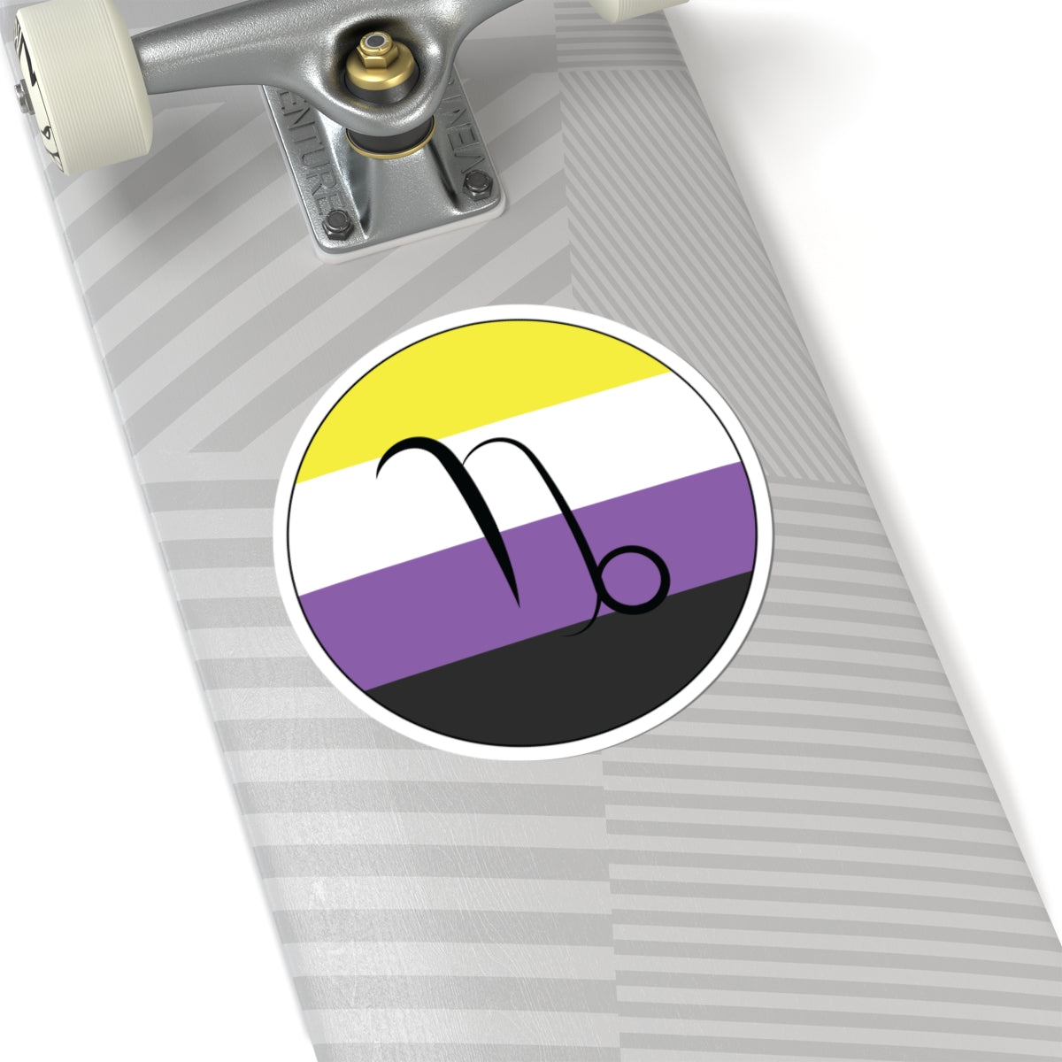 Close-up of the bottom of a silver skateboard featuring a 6 inch by 6 inch circular zodiac sticker with a centered Capricorn glyph on a Nonbinary pride flag style background applied to the surface.