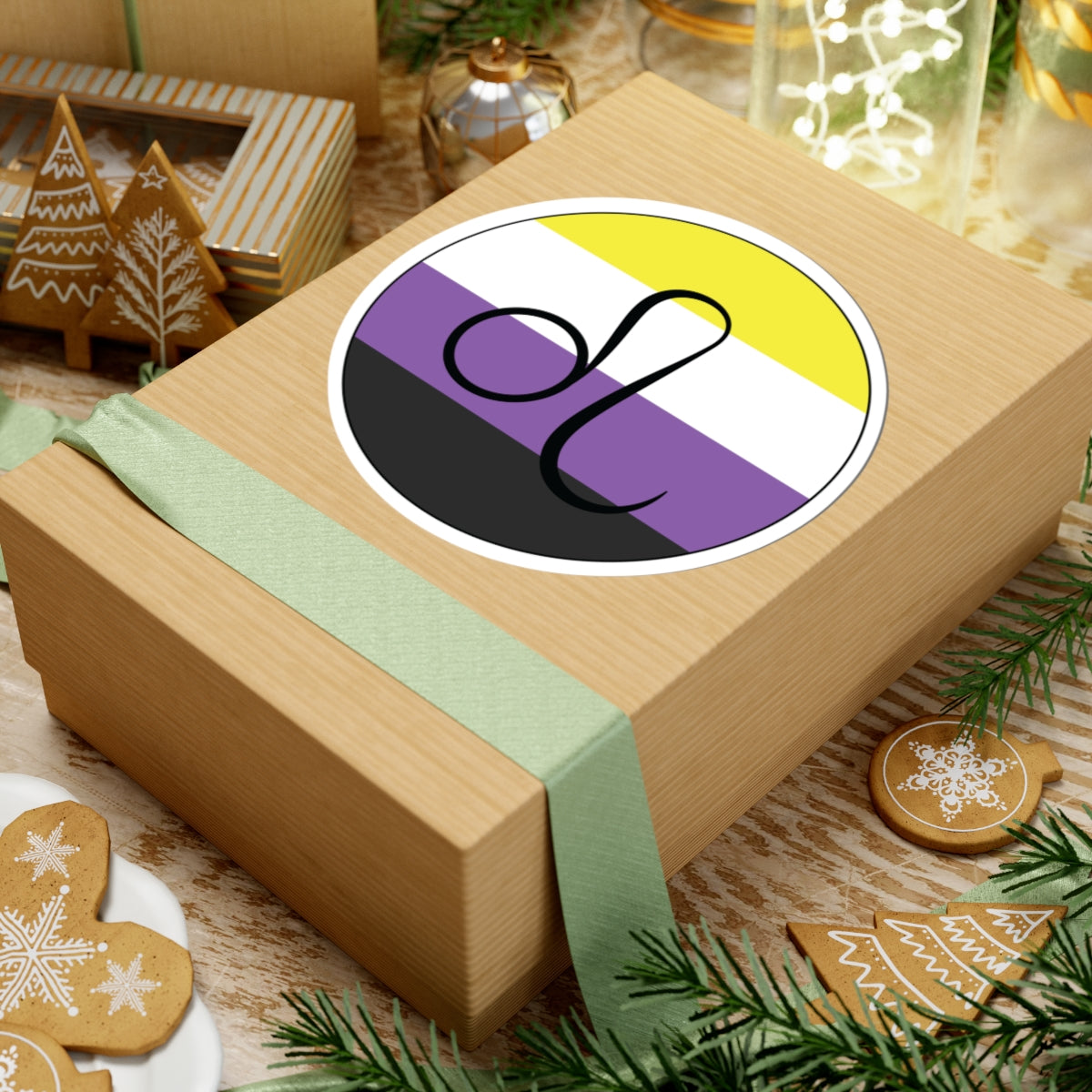 Gift box with a green ribbon on a festive background with cookies and Christmas decorations. Leo Nonbinary pride sticker centered on the box.
