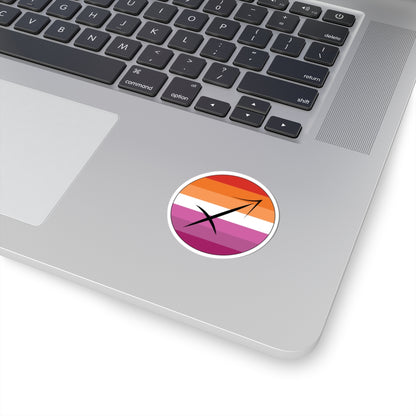 Close-up of the bottom right corner of a silver laptop featuring a 2 inch by 2 inch circular zodiac sticker with a centered Sagittarius glyph on a Lesbian pride flag style background applied to the surface.