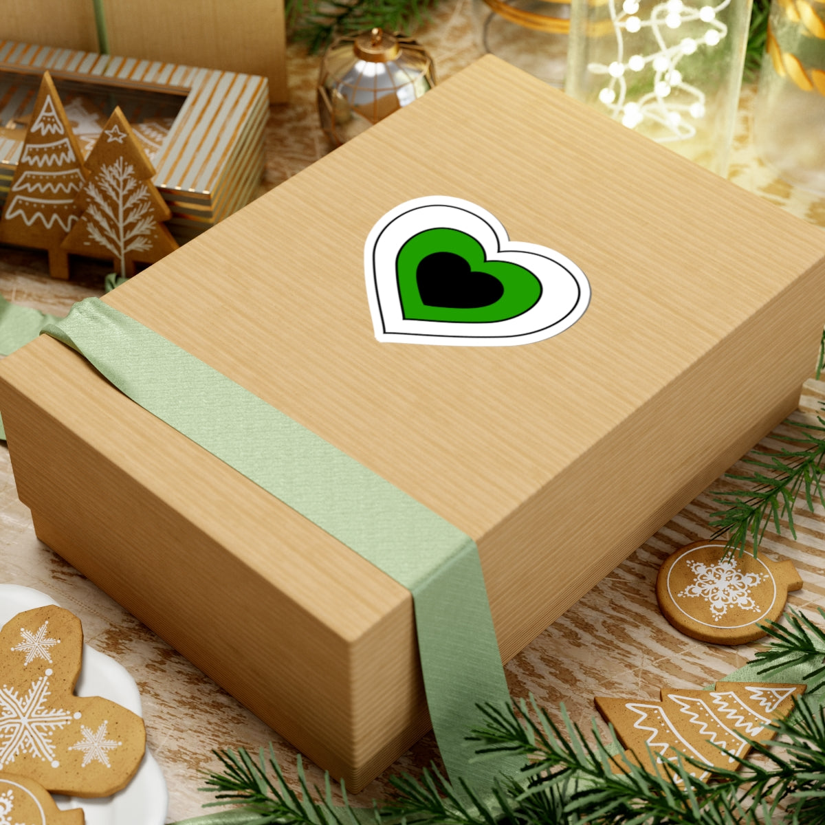 Gift box with a green ribbon on a festive background with cookies and Christmas decorations. Heart-shaped Neutrois pride sticker centered on the box.