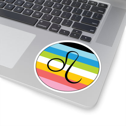 Close-up of the bottom right corner of a silver laptop featuring a 4 inch by 4 inch circular zodiac sticker with a centered Leo glyph on a Queer pride flag style background applied to the surface.