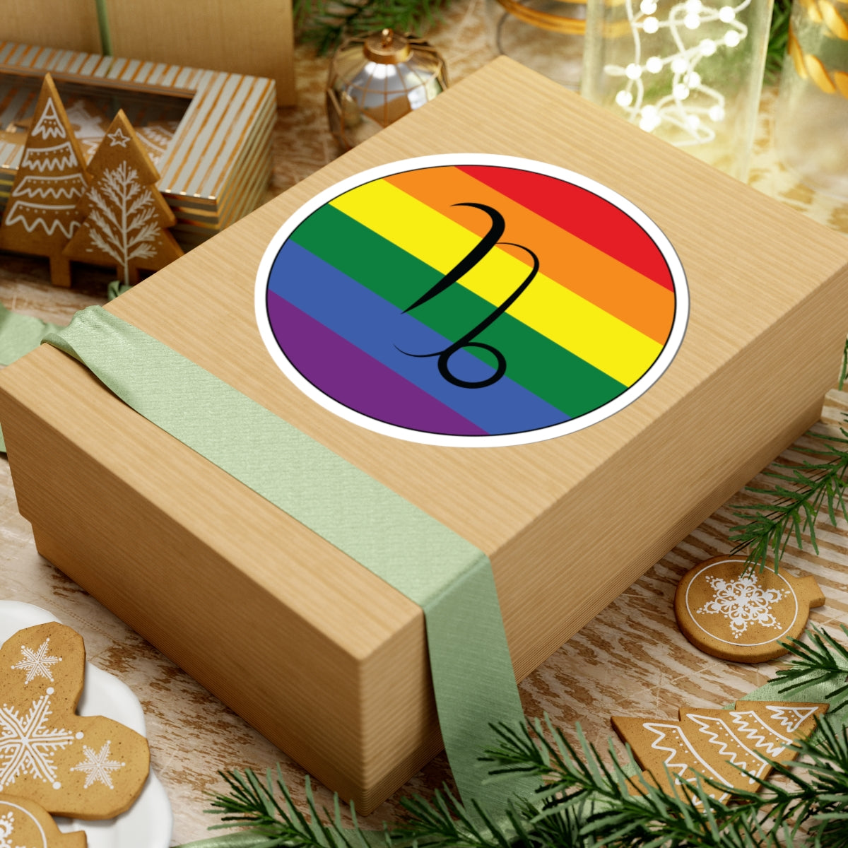 Gift box with a green ribbon on a festive background with cookies and Christmas decorations. Capricorn Rainbow pride sticker centered on the box.