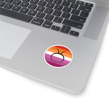 Close-up of the bottom right corner of a silver laptop featuring a 2 inch by 2 inch circular zodiac sticker with a centered Taurus glyph on a Lesbian pride flag style background applied to the surface.