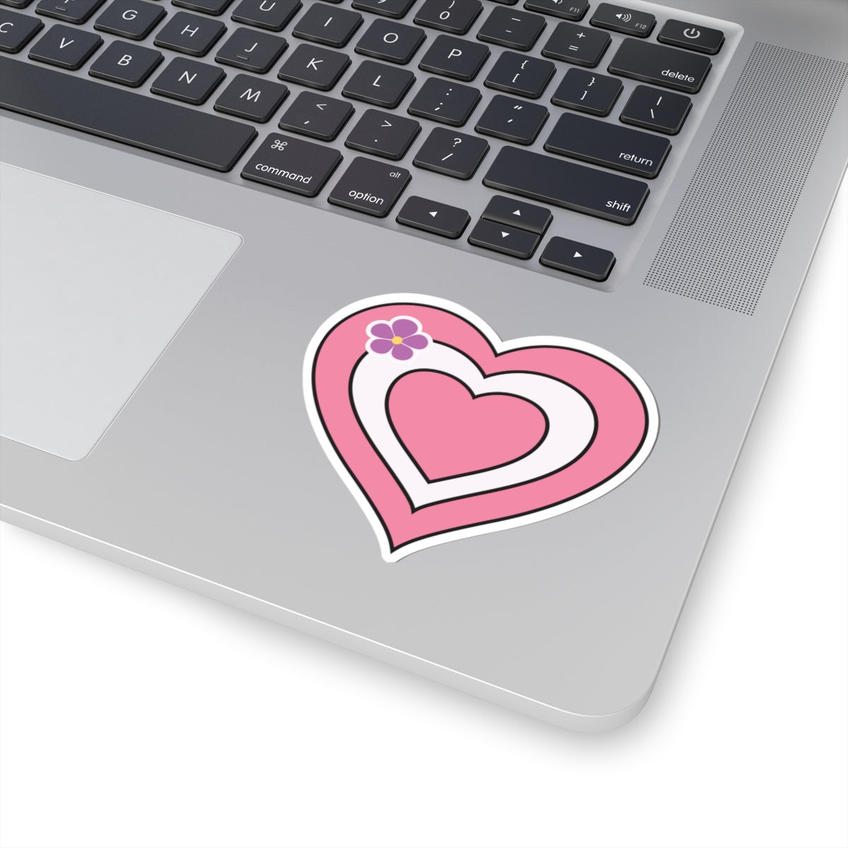 Close-up of the bottom right corner of a silver laptop featuring a 3 inch by 3 inch pride flag heart sticker in a Sapphic pride flag style applied to the surface.