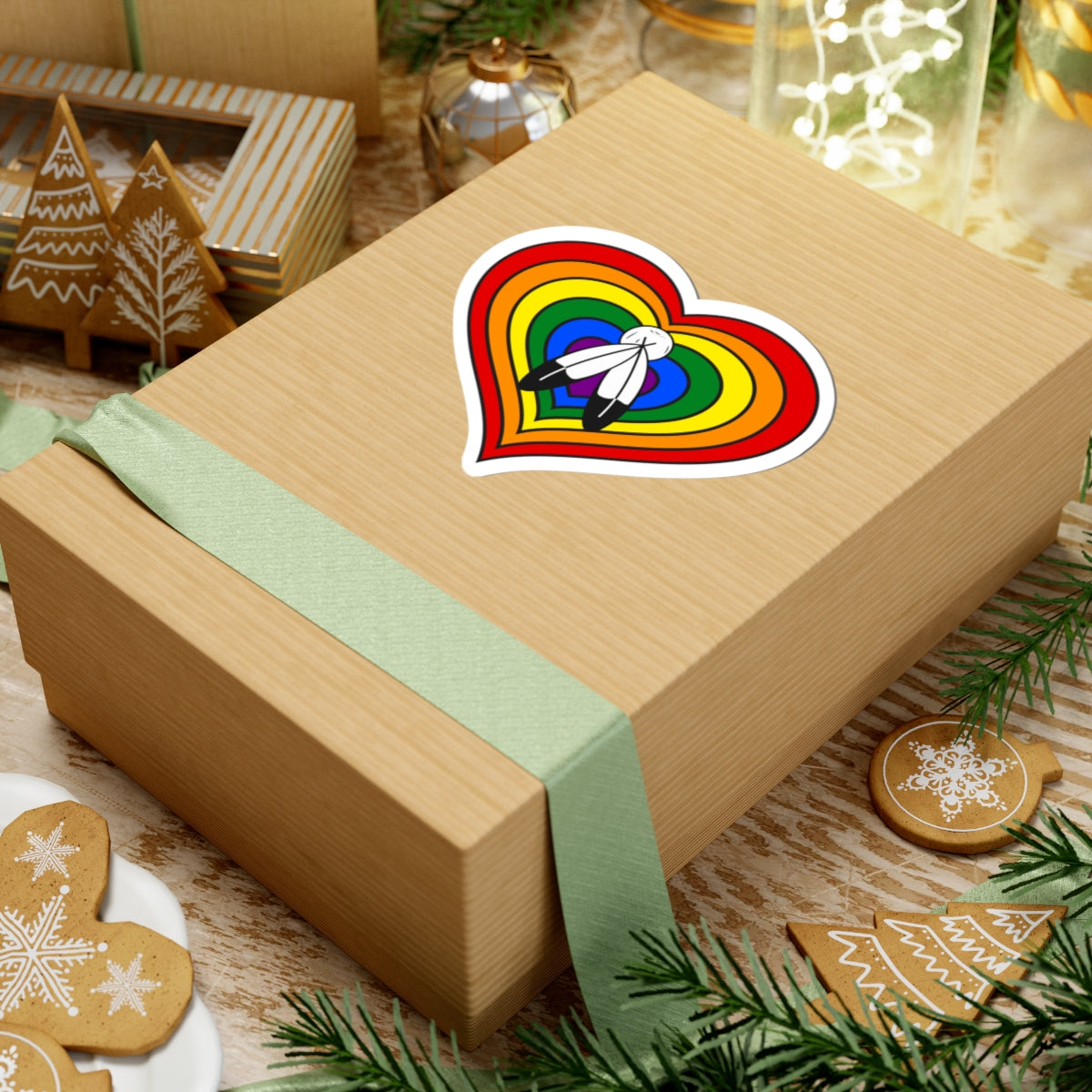 Gift box with a green ribbon on a festive background with cookies and Christmas decorations. Heart-shaped Two-Spirit pride sticker centered on the box.