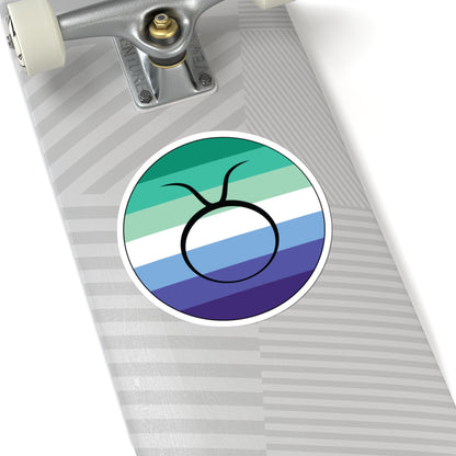 Close-up of the bottom of a silver skateboard featuring a 6 inch by 6 inch circular zodiac sticker with a centered Taurus glyph on a Gay Men pride flag style background applied to the surface.