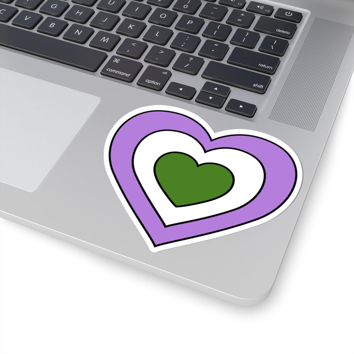 Close-up of the bottom right corner of a silver laptop featuring a 4 inch by 4 inch pride flag heart sticker in a Genderqueer flag style applied to the surface.