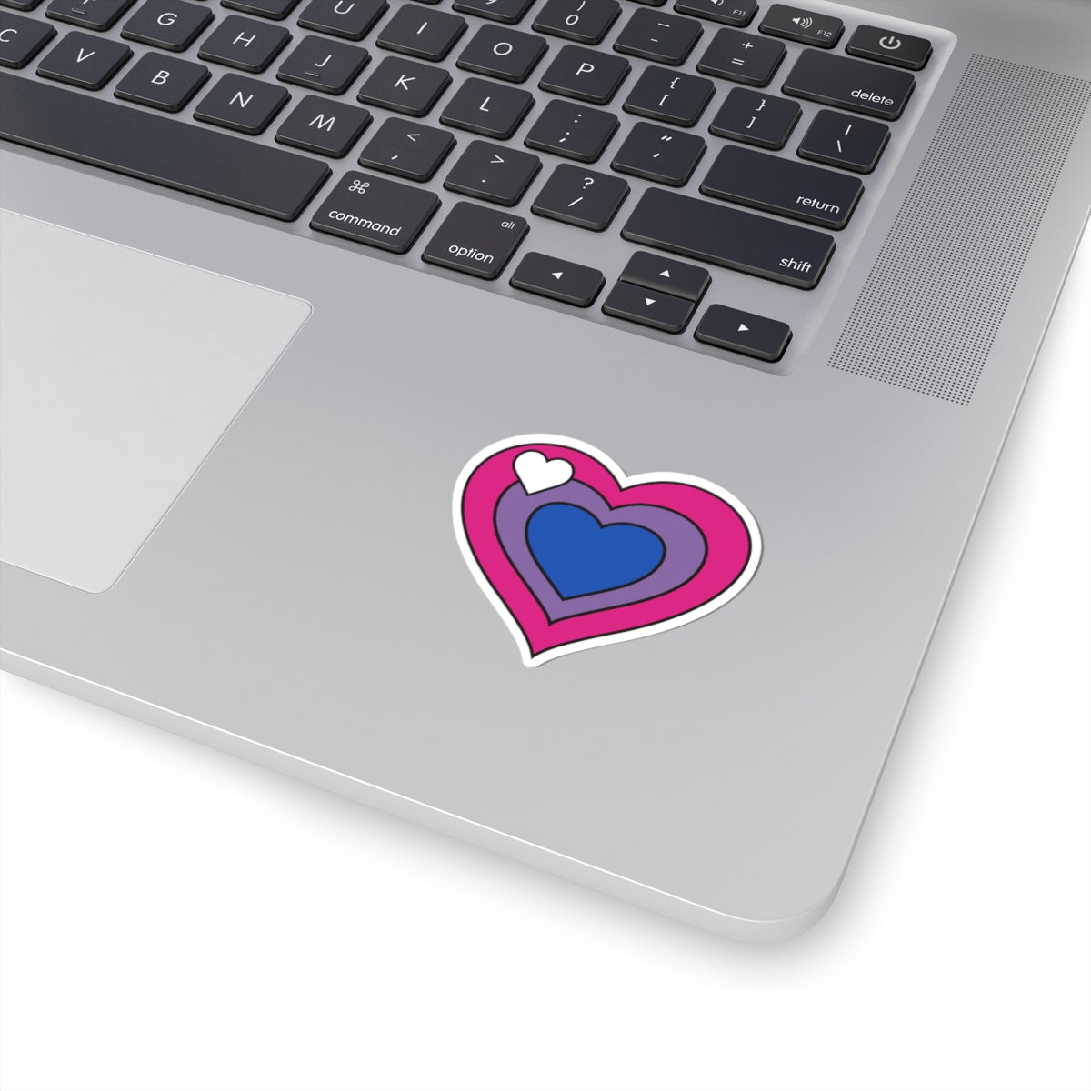 Close-up of the bottom right corner of a silver laptop featuring a 2 inch by 2 inch pride flag heart sticker in a Biromantic flag style applied to the surface.