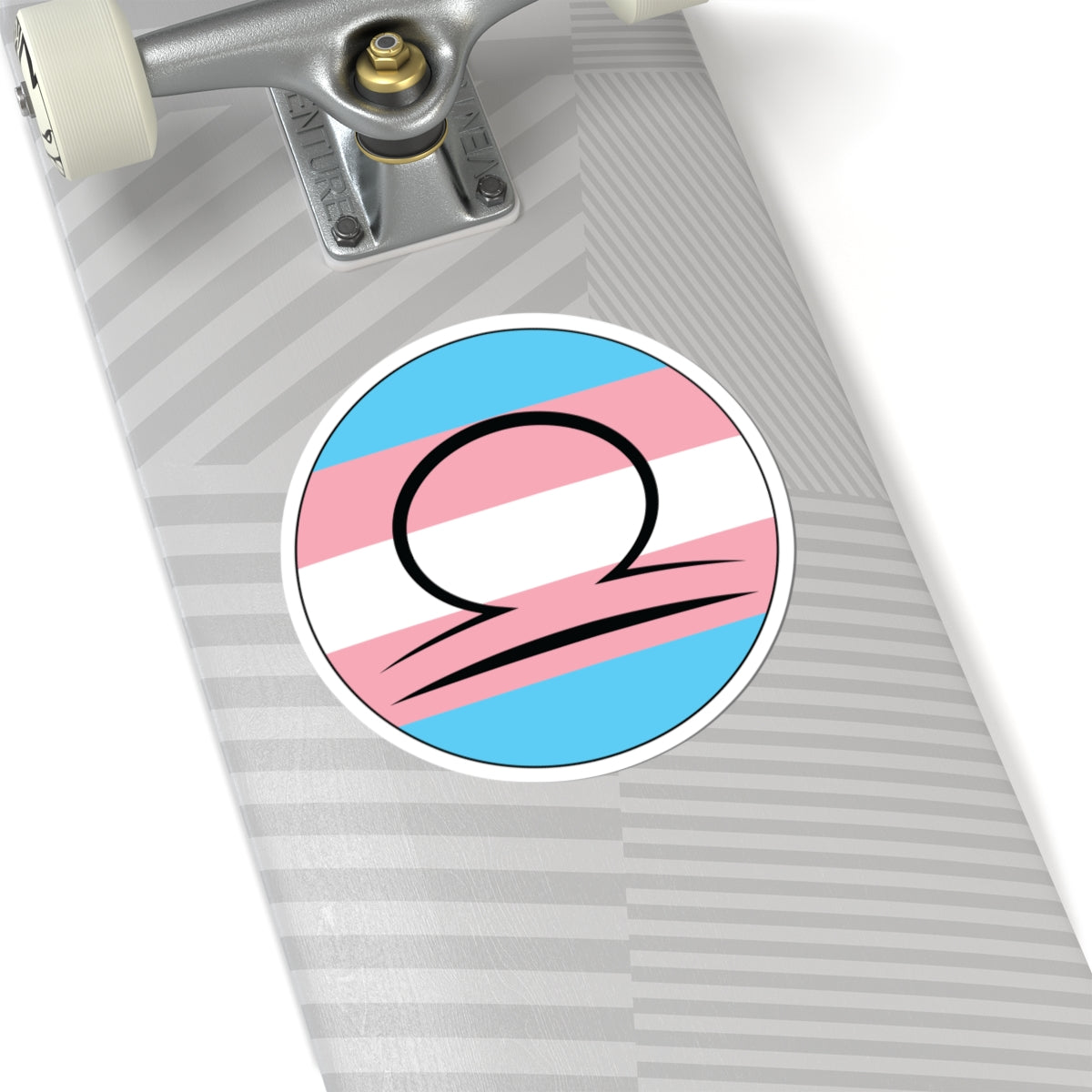 Close-up of the bottom of a silver skateboard featuring a 6 inch by 6 inch circular zodiac sticker with a centered Libra glyph on a Transgender pride flag style background applied to the surface.