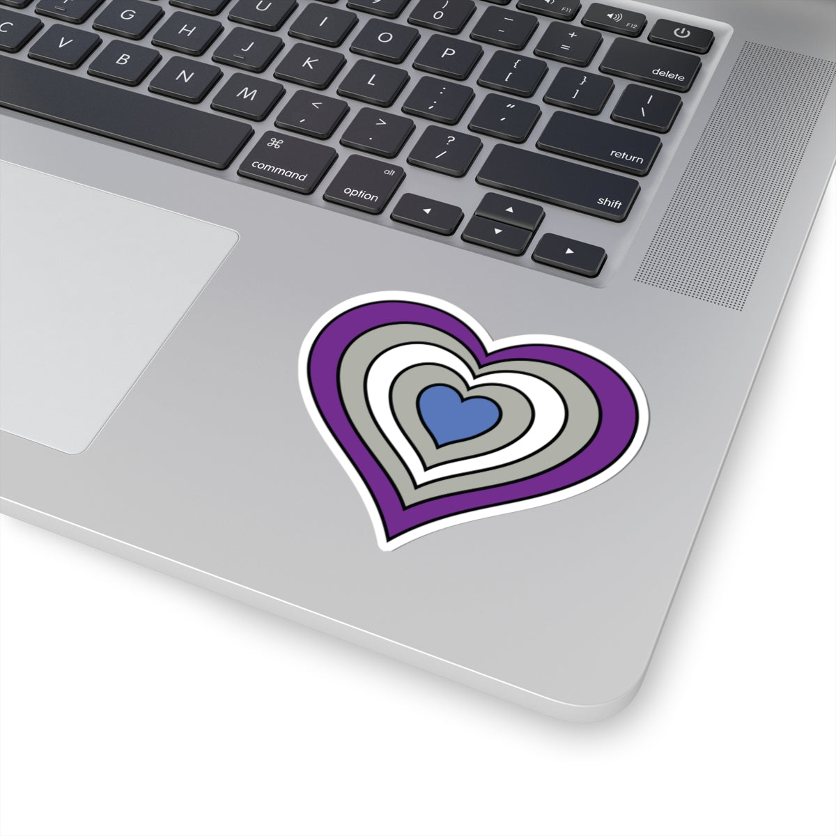 Close-up of the bottom right corner of a silver laptop featuring a 3 inch by 3 inch pride flag heart sticker in a Greysexual flag style applied to the surface.
