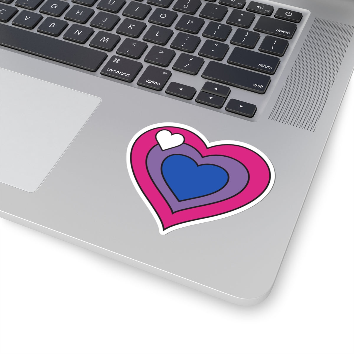 Close-up of the bottom right corner of a silver laptop featuring a 3 inch by 3 inch pride flag heart sticker in a Biromantic flag style applied to the surface.