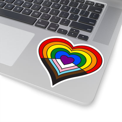 Close-up of the bottom right corner of a silver laptop featuring a 4 inch by 4 inch pride flag heart sticker in a Progress pride flag style applied to the surface.