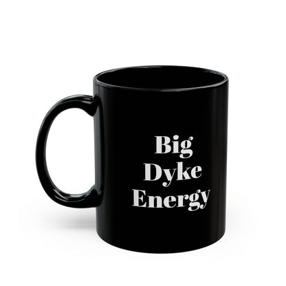 A black mug with the words "Big Dyke Energy" printed in white letters on the side facing outward if the mug is held by the handle in the right hand. The image of the mug is shown on a white background.