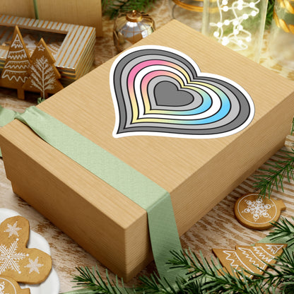 Gift box with a green ribbon on a festive background with cookies and Christmas decorations. Heart-shaped Demifluid pride sticker centered on the box.