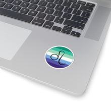 Close-up of the bottom right corner of a silver laptop featuring a 2 inch by 2 inch circular zodiac sticker with a centered Leo glyph on a Gay Men pride flag style background applied to the surface.