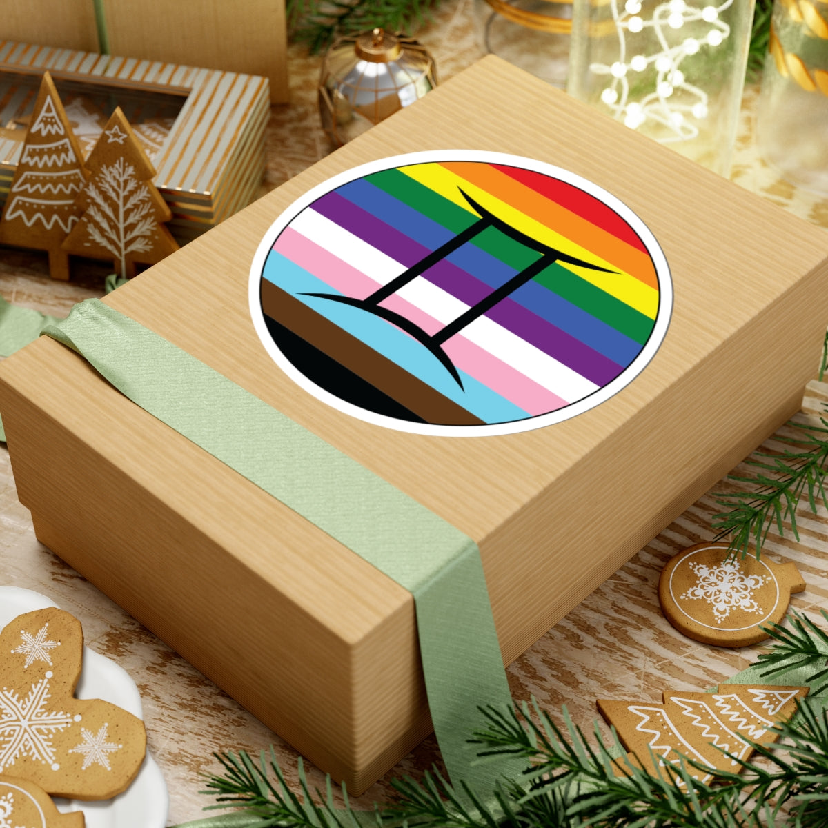 Gift box with a green ribbon on a festive background with cookies and Christmas decorations. Gemini Progress pride sticker centered on the box.