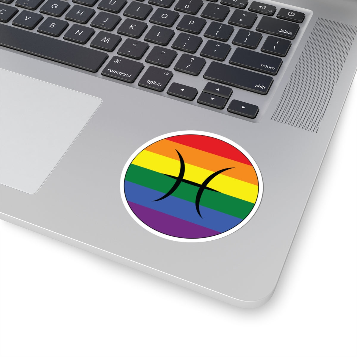 Close-up of the bottom right corner of a silver laptop featuring a 3 inch by 3 inch circular zodiac sticker with a centered Pisces glyph on a Rainbow pride flag style background applied to the surface.